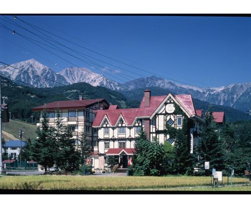 a large house with a red roof with mountains in the background at Rosenheim Hakuba in Hakuba