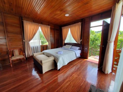 a bedroom with a bed and a chair and windows at CASA BLANCA HORTENCIA in Sucúa