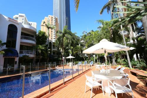 uma piscina com mesas brancas, guarda-sóis e edifícios em St Tropez Resort em Gold Coast