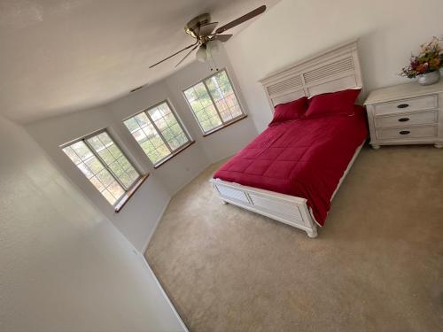 a bedroom with a bed with red sheets and two windows at Kern River Home in Bakersfield