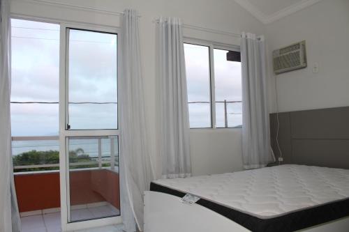 1 dormitorio con 1 cama y 2 ventanas grandes en Praia de Quatro Ilhas a 50 metros do mar, en Bombinhas