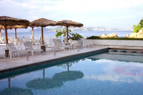una piscina con sedie e ombrelloni accanto all'oceano di Hotel Las Torres Gemelas Acapulco ad Acapulco