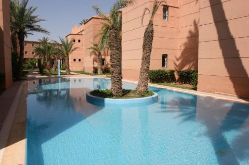 a swimming pool with palm trees and a building at Résidence alqaria assiyahiya in Marrakech