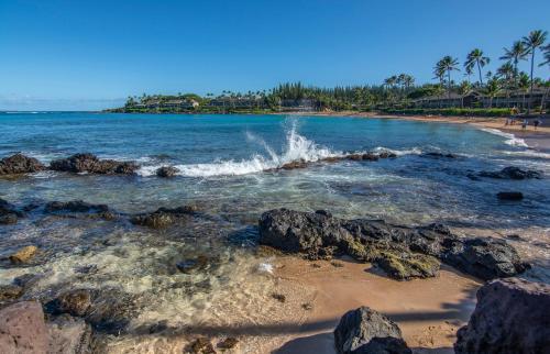 a beach with rocks and water and palm trees at Nāpili Surf Beach Resort by Castle in Lahaina