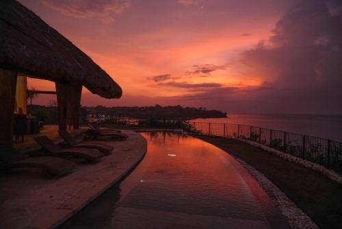 a pool with chairs and a sunset in the background at Villa Tanjung in Nusa Lembongan