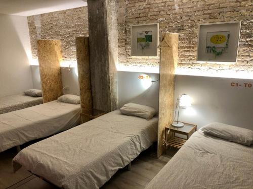 Art&Flats Hostel في فالنسيا: غرفة بثلاث اسرة وجدار من الطوب