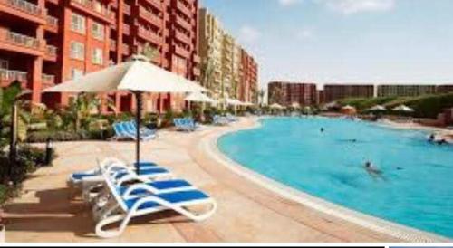a swimming pool with lounge chairs and an umbrella at Amazing view apartment in Golf Porto Marina. in El Alamein