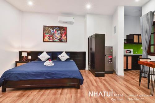 a bedroom with a blue bed and a kitchen at NHATUIshare Quy Nhơn in Quy Nhon