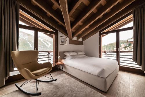a bedroom with a bed and a chair and windows at Chalet Pinnacle in Saas-Fee