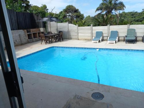 a swimming pool with blue chairs and a table at Poolside Guest House in Port Shepstone