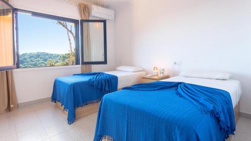 - une chambre avec 2 lits avec des draps bleus et une fenêtre dans l'établissement Villa Coral, à Tamariu