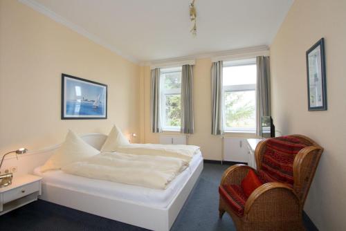 a bedroom with a white bed and a chair at Haus Decker, App 2 in Wenningstedt