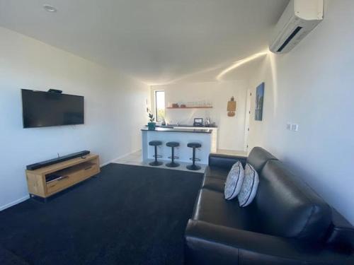 a living room with a black leather couch and a tv at Dune View Accommodation in Mangawhai