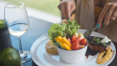 a plate with a bowl of vegetables and a glass of wine at Kembali Hotel Porto de Galinhas - Adults Only in Porto De Galinhas