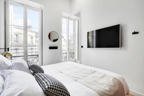 a white bedroom with a bed and a flat screen tv at Maison Labruyère Bordeaux - Jardin Public in Bordeaux