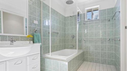 La salle de bains est pourvue d'une baignoire, d'un lavabo et d'une douche. dans l'établissement Coconuts - 2 balconies and stroll to choice of 2 beaches, à Nelson Bay