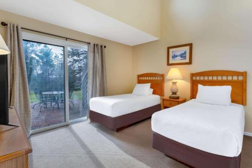 a bedroom with two beds and a sliding glass door at Tamarack Wisconsin Dells, a Ramada by Wyndham in Wisconsin Dells