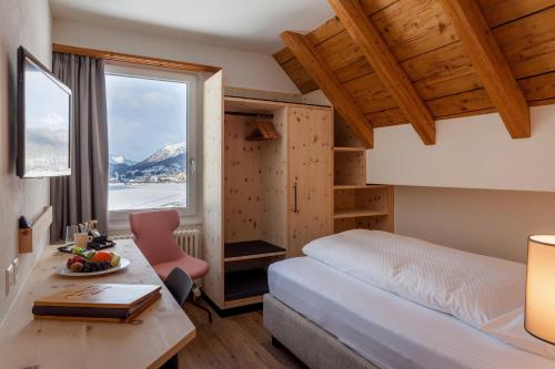 Habitación de hotel con cama, escritorio y ventana en Hotel Waldhaus am See en St. Moritz