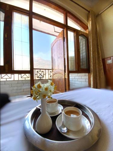 a tray with two cups of coffee and a vase with flowers at Hotel Sanjeevny in Bajaura