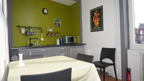 een keuken met een tafel en stoelen en een groene muur bij Abri du Passant in Roubaix
