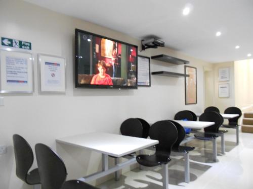 a waiting room with tables and chairs and a tv on the wall at Mapesbury Hostel London in London