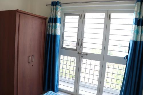 a room with two large windows with blue curtains at Nature's Lap Homestay in Igatpuri