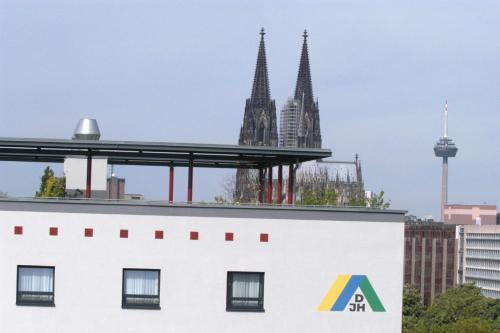 a building with a logo on it in front of two towers at Jugendherberge Köln-Deutz in Cologne