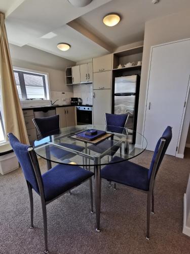 a glass table and chairs in a room with a kitchen at The Anchorage Apartments in Mount Maunganui