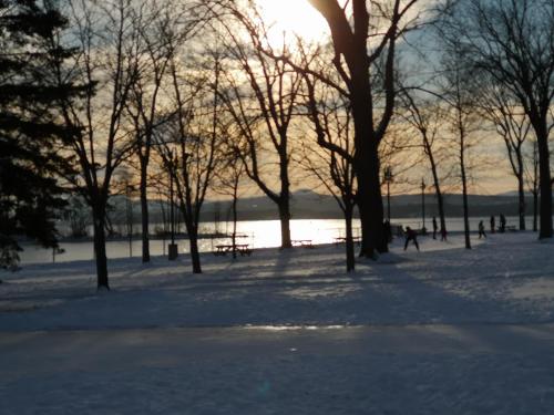 a park covered in snow with the sun setting in the background at Condo de L'Oberge in Magog-Orford