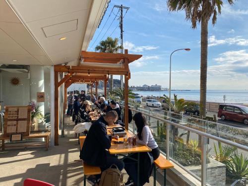 a group of people sitting at tables in a restaurant overlooking the ocean at GOOD MORNING ZAIMOKUZA in Kamakura