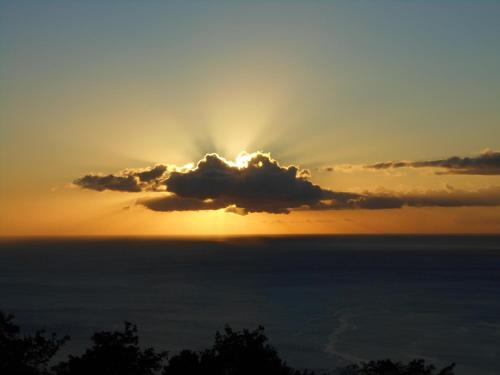 a sun setting behind a cloud over the ocean at Diamond View Cottages in Roseau