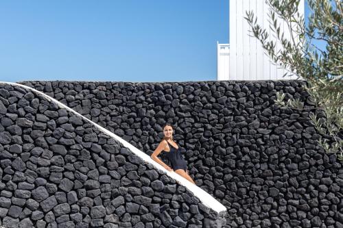 a woman in a black dress sitting on a surfboard at Santa Irina Luxury Sunny Lofts in Perivolos