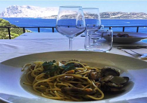 a plate of pasta on a table with wine glasses at SAN TEODORO PUNTA EST AMPIO TRILOCALE VISTA MARe in Capo Coda Cavallo