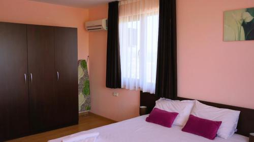 a bedroom with a bed with purple pillows and a window at Вила Делфин - Villa Delfin in Bŭlgarevo