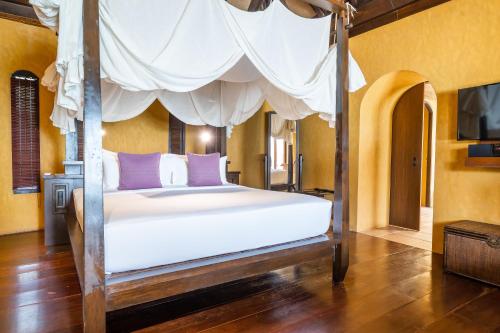 a bedroom with a canopy bed with white sheets and purple pillows at Paradee in Ko Samed
