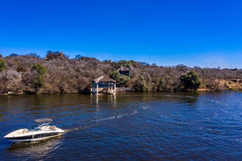 a small boat on the water with a house in the background at Vaal River YOLO Spaces - Vaal River Bush Villa in Sasolburg