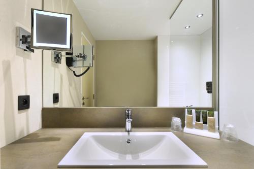 a bathroom with a sink and a tv on the wall at Hotel Charleroi Airport - Van Der Valk in Charleroi