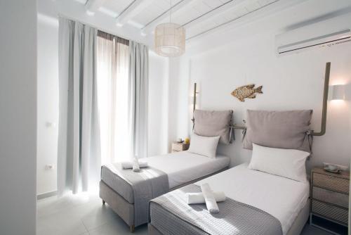 a white bedroom with two beds and a chair at Desire Mykonos Apartments in Vrisi/ Mykonos