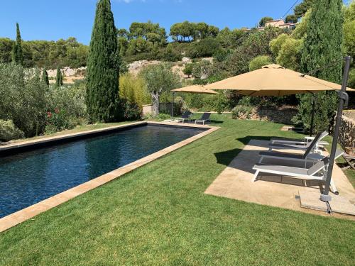 a swimming pool with chairs and an umbrella next to a yard at Le Clos de la Chèvre Sud in La Cadière-dʼAzur