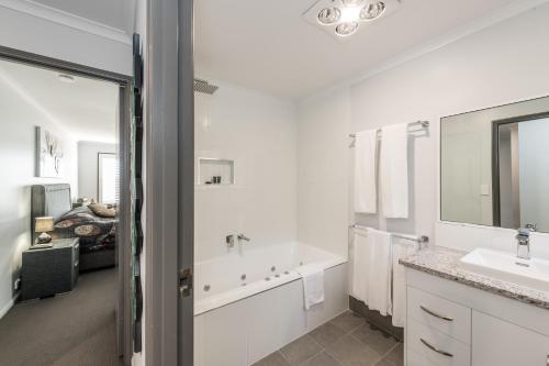 Baño blanco con bañera y lavamanos en Athena Motel Apartments en Toowoomba