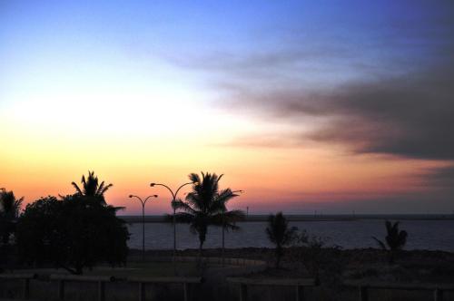 a sunset on the beach with palm trees and the ocean at Hospitality Port Hedland in Port Hedland
