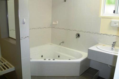 a white bathroom with a tub and a sink at Shady Rest Motel in Gympie