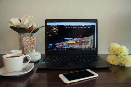 a laptop computer sitting on a wooden table with a cell phone at Casablanca Suites Near Airport in Legazpi