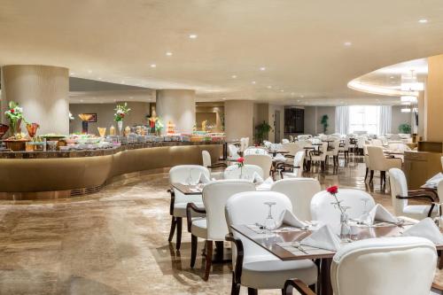 ein Restaurant mit weißen Tischen und Stühlen und einer Bar in der Unterkunft Copthorne Makkah Al Naseem in Mekka