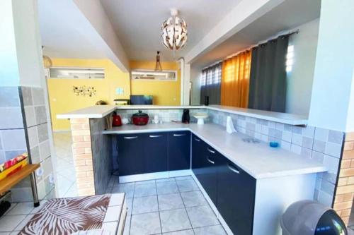 eine Küche mit blauen Schränken, gelben Wänden und einem Kronleuchter in der Unterkunft Charmant appartement avec piscine in Le Robert