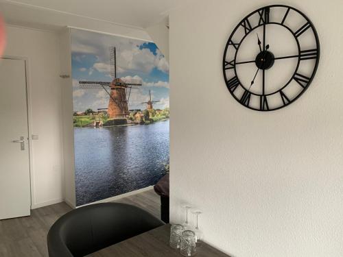 a clock on a wall with a painting of a windmill at Slapen bij de Buurvrouw in Castricum