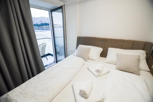 a bed with white sheets and pillows and a window at Villa San Antonio 3-PALADA in Baška