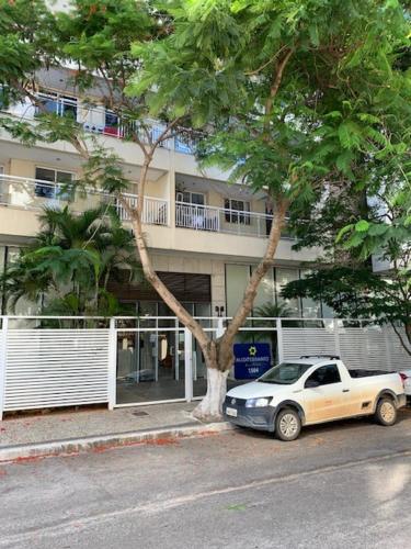 ein weißes Auto, das neben einem Baum vor einem Gebäude parkt in der Unterkunft Apartamento para família moderno e prático próximo a belas praias in Cabo Frio
