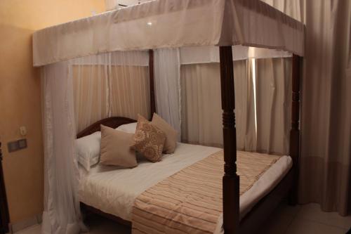 une chambre avec un lit à baldaquin avec des draps et des oreillers blancs dans l'établissement Moffat Court Boutique Hotel, à Mombasa