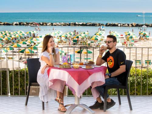 a man and woman sitting at a table in front of the beach at Hotel Villa Sole Resort in Bellaria-Igea Marina